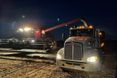 Combine offloads to a grain truck as harvest invades nightfall